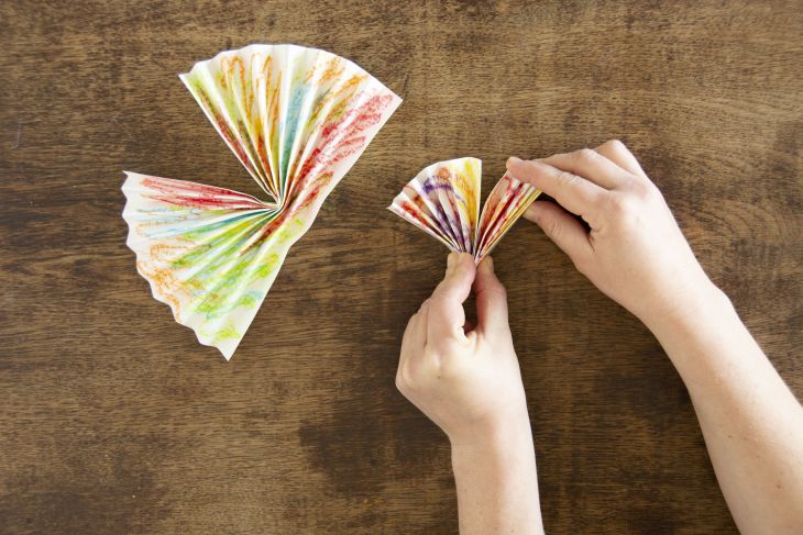 Jemand knickt zwei selbstgefaltete Papierfächer in der Mitte.