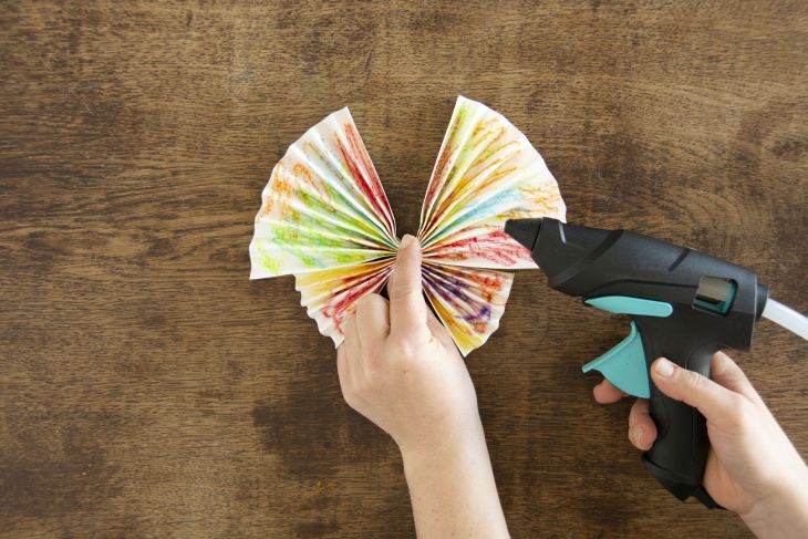 Jemand verbindet zwei selbstgefaltete Papierfächer mit Hilfe einer Heißklebepistole.