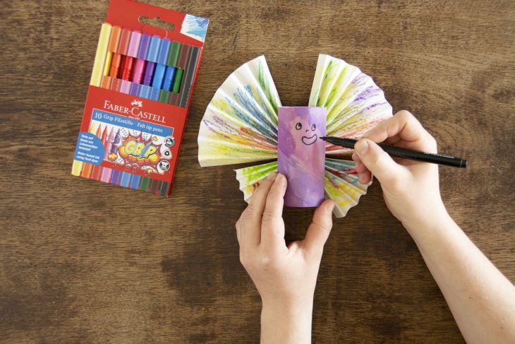 Jemand malt ein Gesicht auf einen selbstgebastelten Schmetterling.