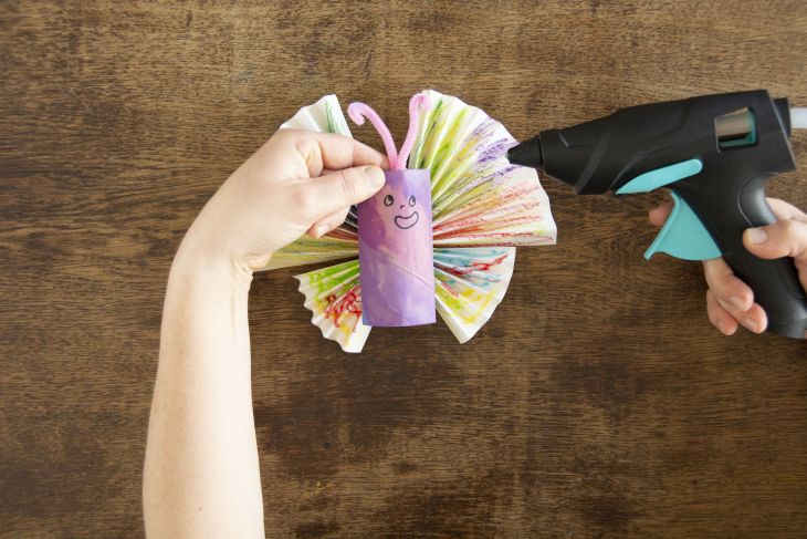 Jemand klebt Pfeifenputzer als Fühler an einen selbstgebastelten Schmetterling