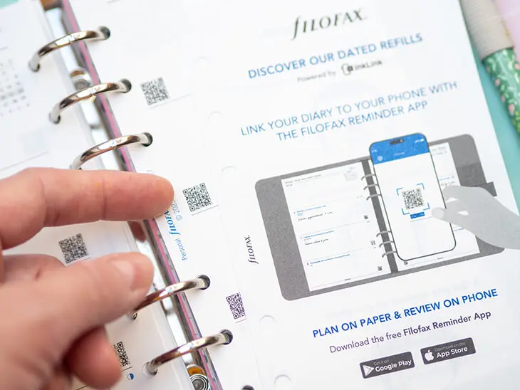 Jemand zeigt mit dem Finger auf einen QR-Code in einem Filofax Planner. Daneben liegt ein Blatt mit der Anleitung für die Filofax-Reminder-App. Foto: Johanna Rundel