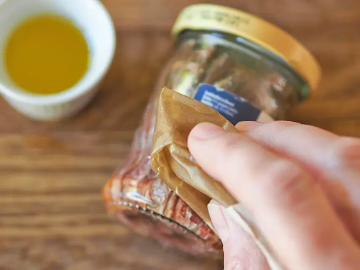 Jemand reibt das Papieretikett eines Glases mit Speiseöl ein, um das Etikett zu entfernen. Foto: Johanna Rundel