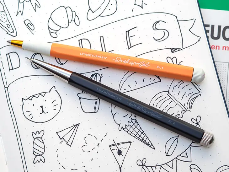 Ein orangener Drehgriffel No.1 und ein schwarzer Drehgriffel No.2 von LEUCHTTURM1917 liegen auf einer BuJo-Seite mit Doodles. Foto: Johanna Rundel