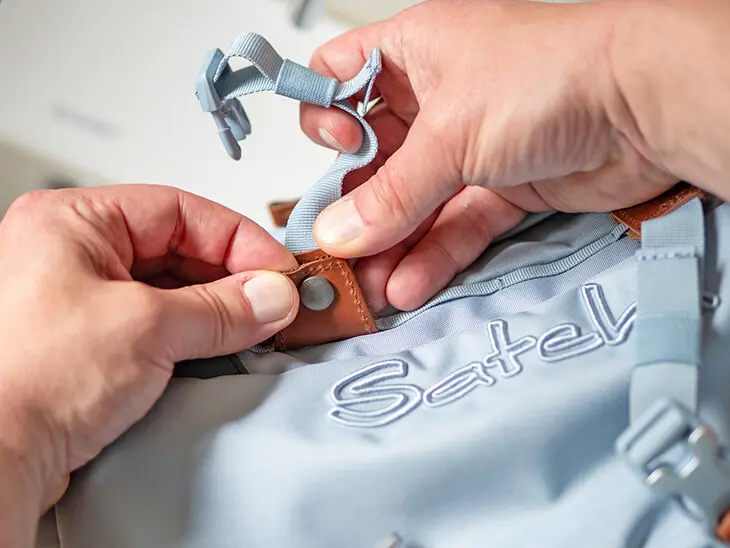 Jemand entfernt die Swaps an einem hellblauen Schulrucksack von satch. Foto: Johanna Rundel