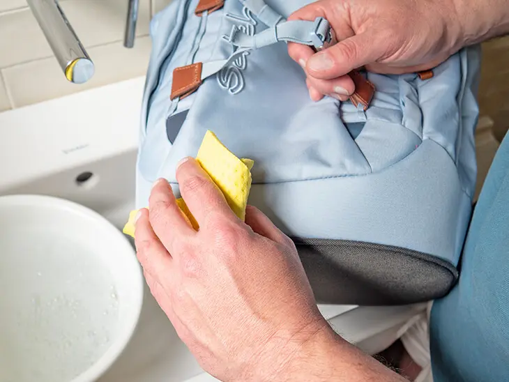 Jemand reibt die Außenseite eines hellblauen Schulrucksacks von satch mit einem weichen Tuch ab, um ihn zu reinigen. Foto: Johanna Rundel