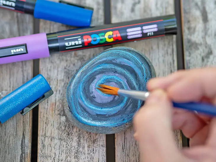 Jemand verblendet POSCA-Marker mit einem Pinsel auf einem Stein. Foto. Johanna Rundel