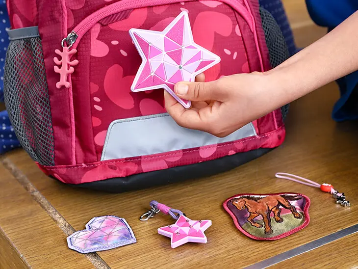 Ein Kind befestigt ein Magic Mag in Sternform an einem pinken Schulranzen von Step by Step.
