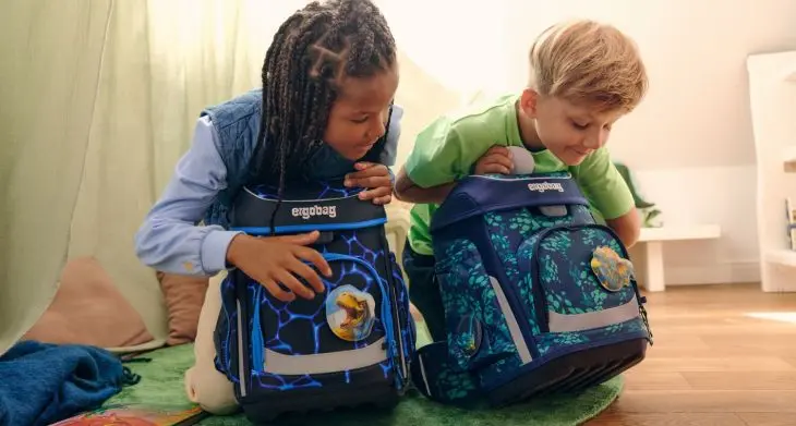 Zwei Kinder sitzen auf dem Boden und beugen sich über ihre Schulranzen von ergobag