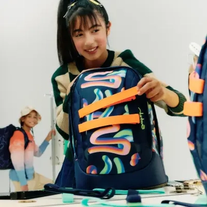 Ein Mädchen zieht an den Frontloops ihres bunten satch pack Rucksacks