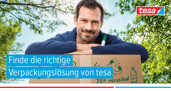 Ein lächelnder Mann lehnt im Freien an einem großen Karton, der mit tesapack® verschlossen ist und hält einen Marker in der Hand. Im Hintergrund sind Bäume und ein klarer Himmel zu sehen.