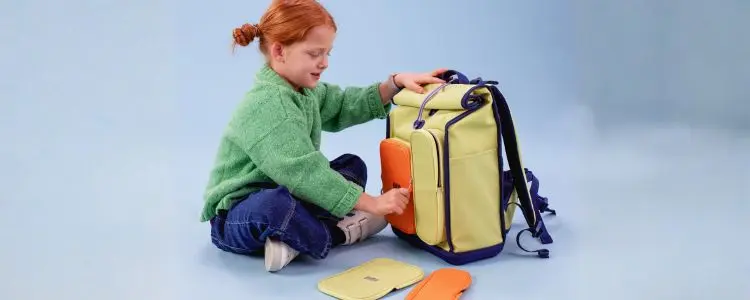 Ein Kind sitzt im Schneidersitz auf dem Boden und öffnet gerade einen Schulranzen von KWIO