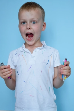 Kind mit bemaltem T-Shirt hält bunte Filzstifte in der Hand