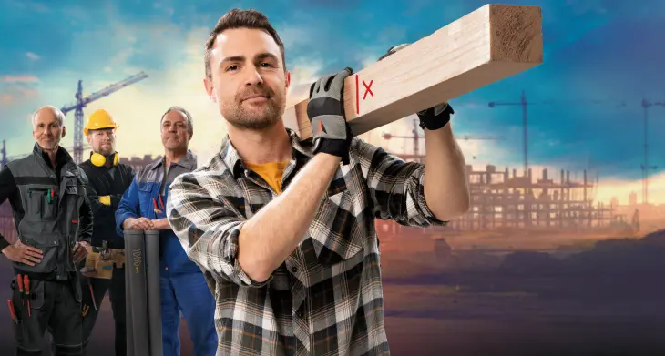 Eine Gruppe von vier Bauarbeitern steht in einer Reihe, in der Mitte hält ein Mann ein großes Holzbrett. Sie tragen verschiedene Baukleidungen, darunter Helme und Overalls. 