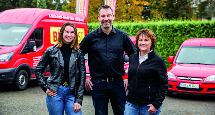 Drei Personen stehen vor roten Autos.