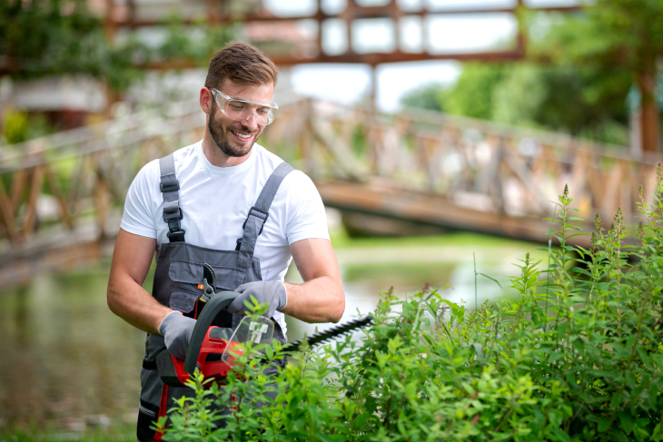 Ein Mann schneidet eine Hecke.