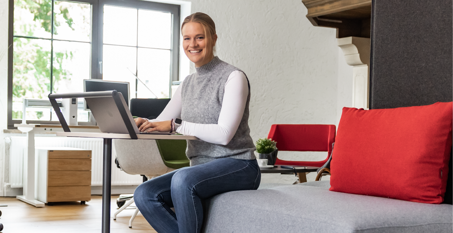 Eine Frau sitzt mit einem Notebook an einem mobilen Beistelltisch in einem Büro.