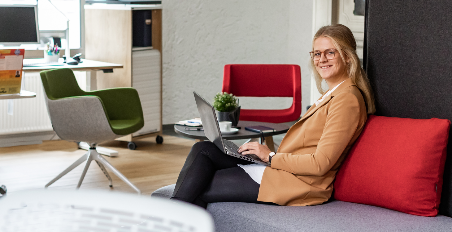 Eine Frau sitzt mit ihrem Notebook in einem Loungebereich.