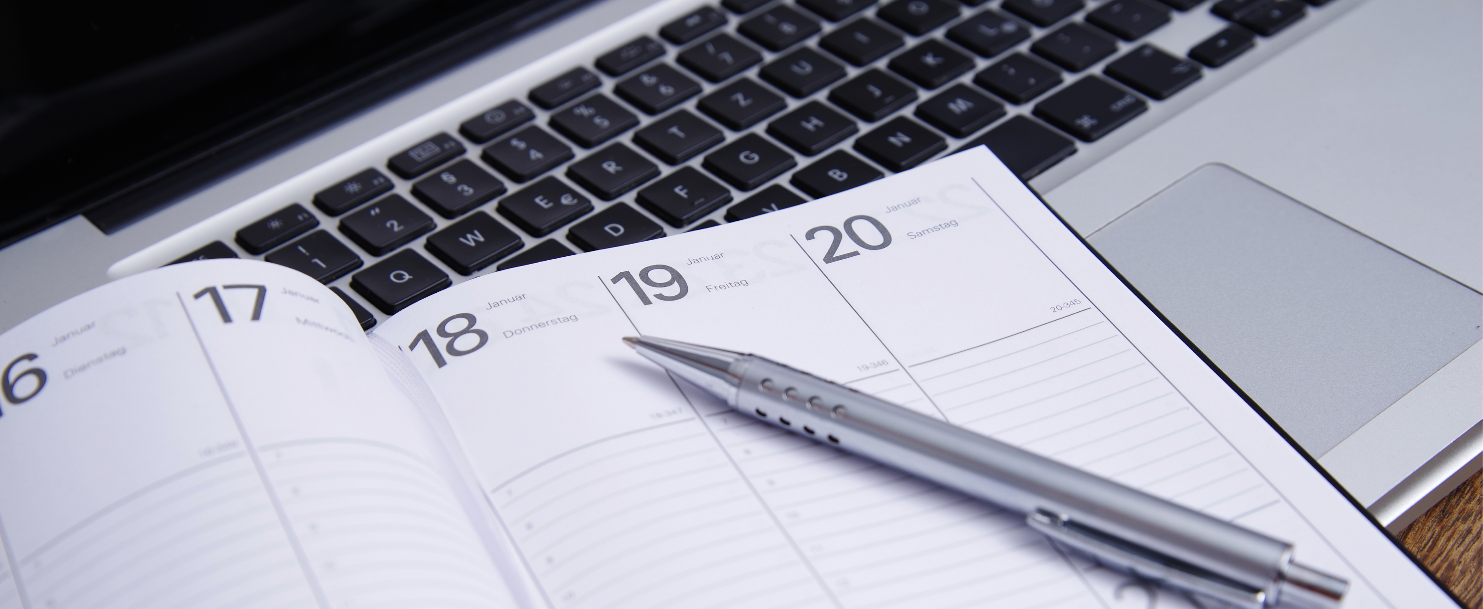 Buchkalender und ein Kugelschreiber, welche auf einem Notebook liegen.