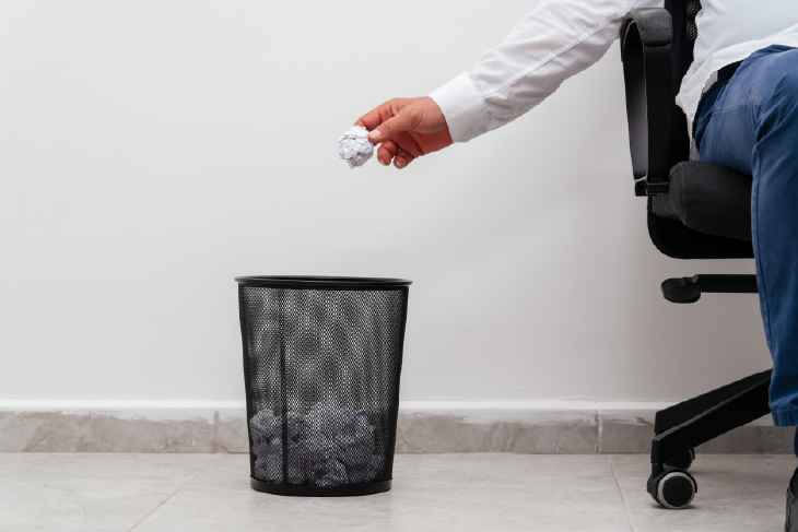 Eine Person schmeißt Papier in einen Papierkorb.