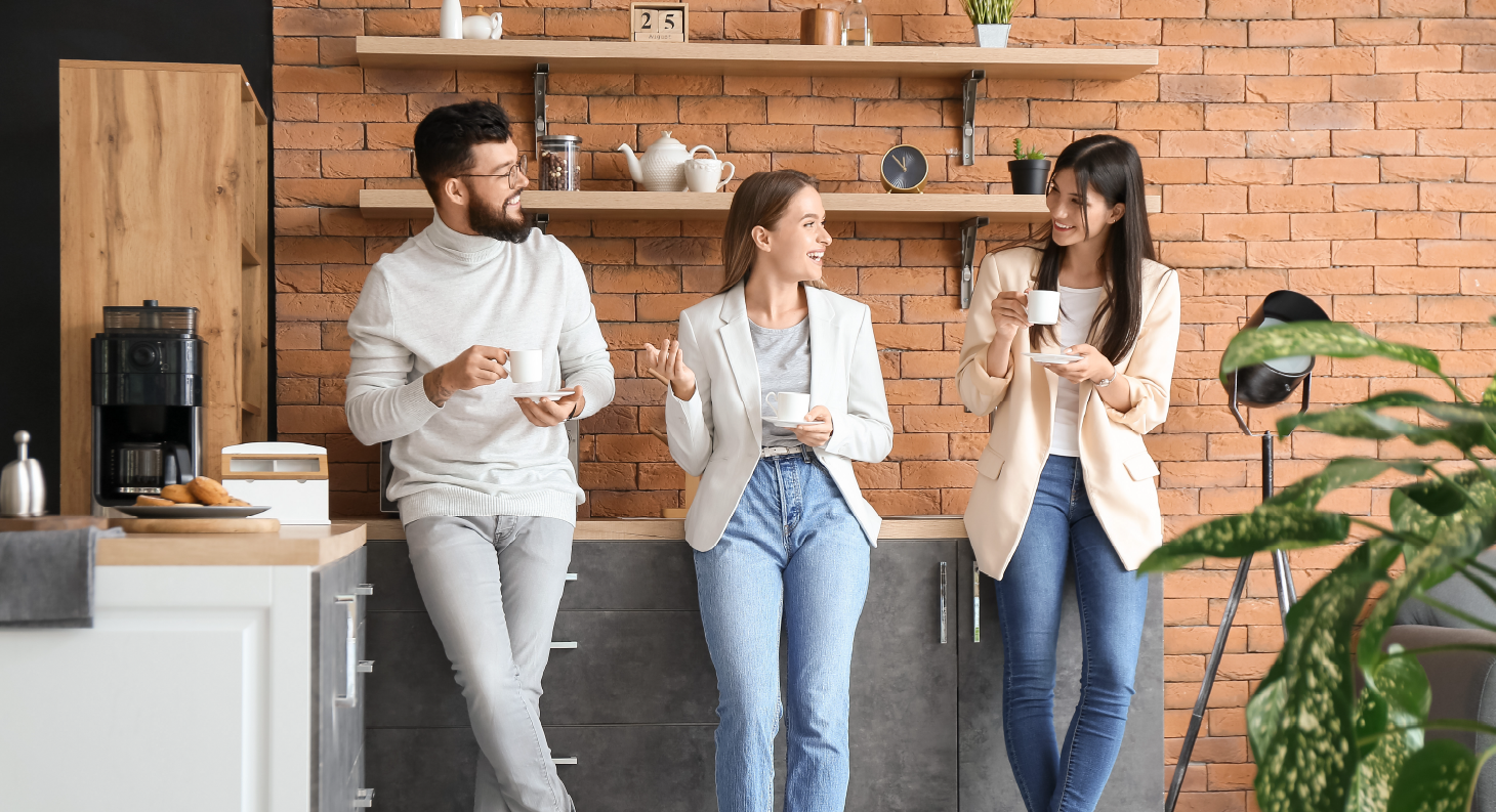 Drei Personen stehen in einer Büroküche und trinken Kaffee.