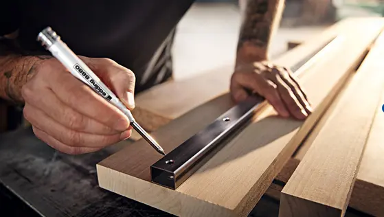 Das Bild zeigt einen Mann, der mit einem edding Tiefloch Baumarker ein Loch auf einem Holzstück anzeichnet. Auf dem Holz liegt eine Metallschiene mit Löchern.