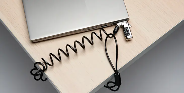 Das Bild zeigt ein Laptop, das mit einem Kabelschloss an einem Tisch gesichert ist. Das spiralförmige Sicherheitsschloss bietet Schutz vor Diebstahl und sorgt für eine zuverlässige Sicherung.