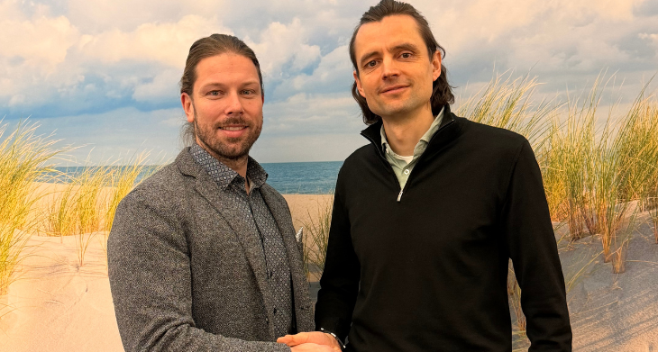 Zwei Männer schütteln sich die Hand, im Hintergrund ist ein Strand zu sehen.