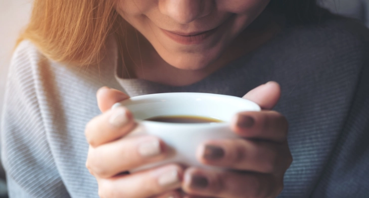 Frau genießt lächelnd eine heiße Tasse Kaffee