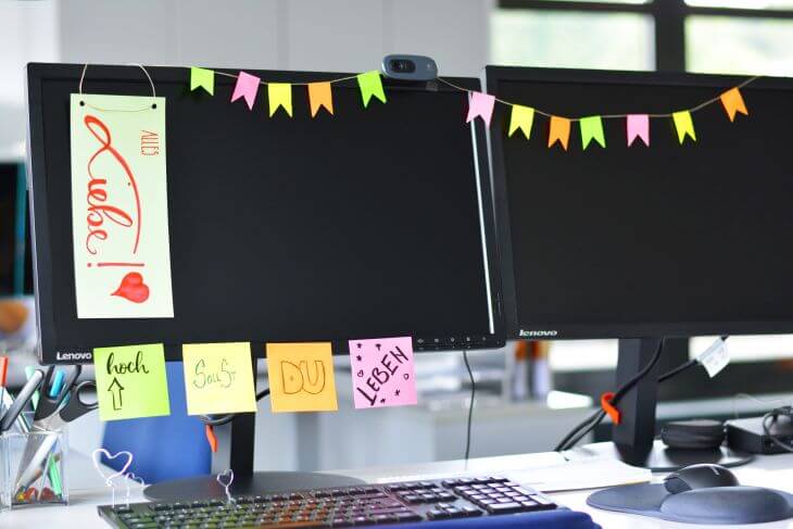 Ein Computerbildschirm ist mit einer Wimpelkette aus Haftnotizblättern behangen. Außerdem kleben daran vier beschriftete Notizblätter mit den Worten "Hoch sollst du leben". Auf einem Trennstreiften ist "Alles Liebe" gelettert.