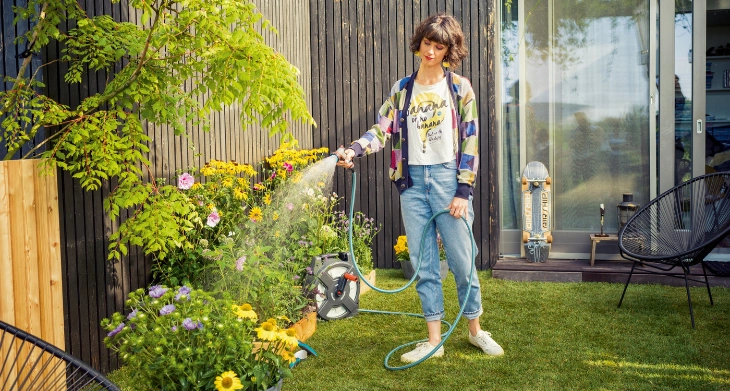 Frau bewässert Blumenbeet im Garten mit Gartenschlauch.
