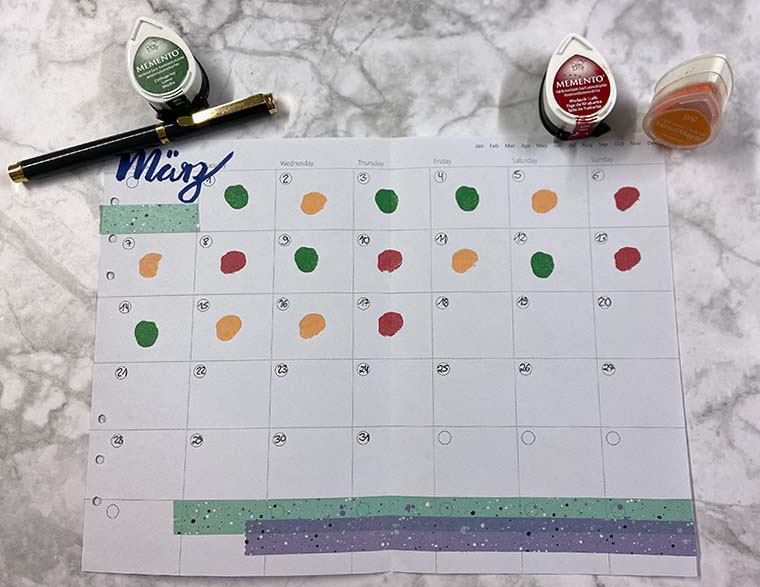 Mit Stempeln wurde in eine Monatsübersicht als Moodtracker umfunktioniert. Am oberen Bildrand liegen drei Sempelkissen sowie ein Kugelschreiber der Marke Filofax.