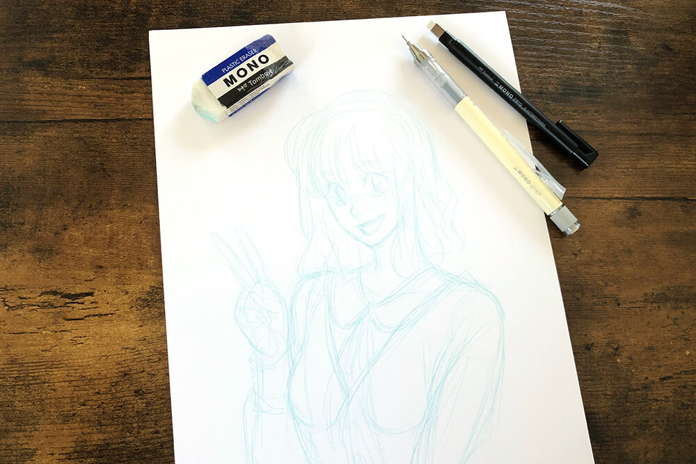 Auf einem braunen Holztisch liegt ein Blatt Papier. Darauf wurde mit blauer Bleistiftmine die Skizze einer jungen Frau im Manga-Stil gezeichnet. Außerdem sind folgende Materialien von Tombow auf dem Bild zu sehen: Radiergummi und Bleistifte. Foto: Reyhan Yildirim
