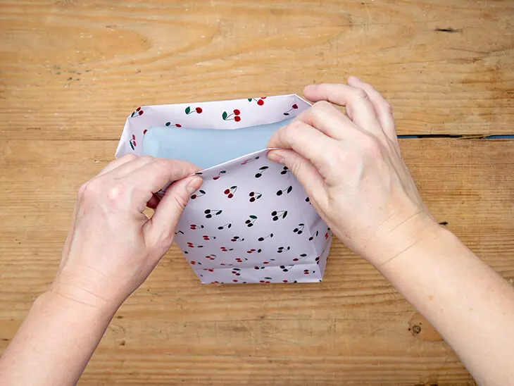 Jemand faltet eine Geschenktüte aus einem Geschenkpapier von STEWO. Foto: Johanna Rundel