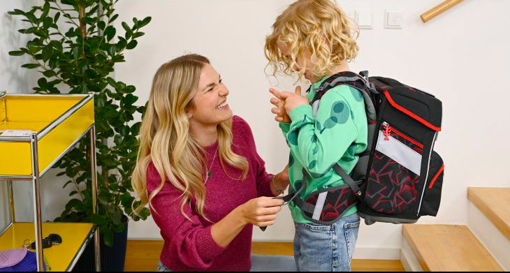 Eine Mutter kniet vor ihrem Kind und hilft ihm, einen Schulranzen von Step by Step anzuziehen