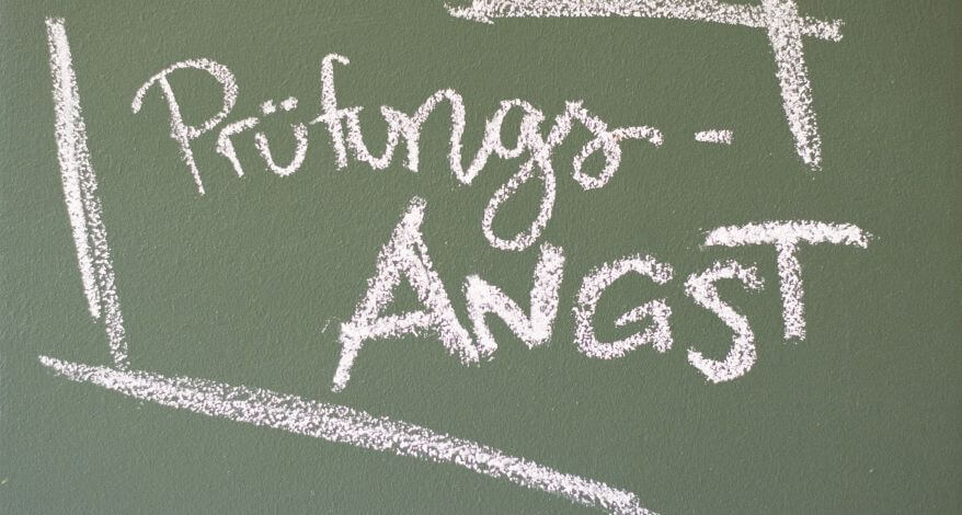 Auf einer grünen Tafel wurde mit weißer Kreide das Wort "Prüfungsangst" geschrieben. Das Wort wird mit einzelnen weißen Strichen umrandet.