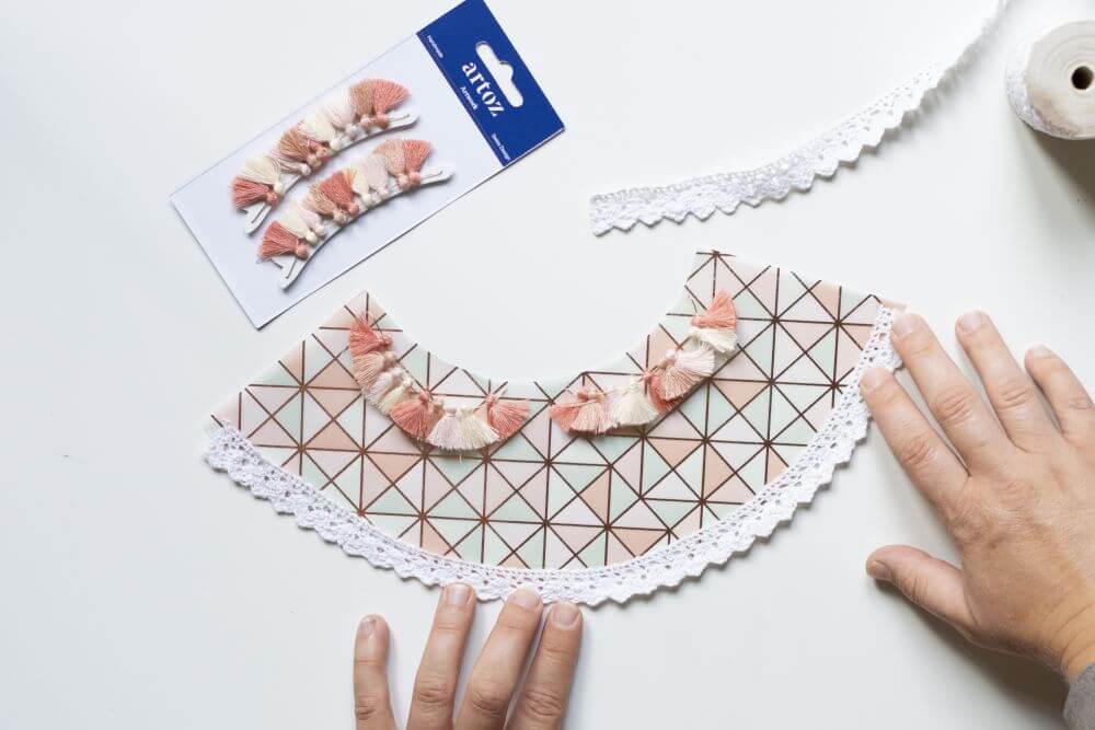 Ein Halbkreis aus buntem Transparentpapier wird mit Troddeln und Spitze beklebt.