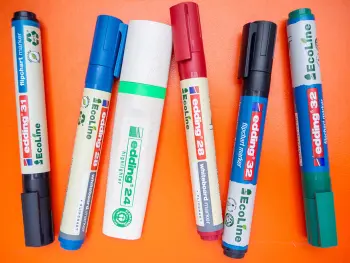 Mehrere Permanent- und Flipchart-Marker, sowie ein Highlighter der EcoLine von edding liegen auf einem orangenen Untergrund. Foto: Johanna Rundel