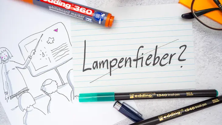 Neben eine Skizze einer Person, die etwas an einem Flipchart präsentiert, liegt eine Karteikarte mit dem durchgestrichenen Wort „Lampenfieber“. Drumherum sind einige Stifte von edding verteilt. Foto: Johanna Rundel
