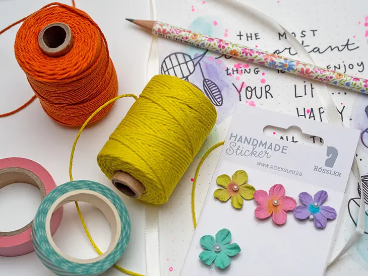 Washitape, Bäckergarn und Aufkleber von Rössler liegen auf einer aufgeschlagenen Bullet Journal Seite. Foto: Johanna Rundel