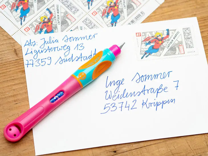 Auf einem adressierten weißen Briefumschlag mit Briefmarke liegt ein bunter Griffix-Schreiblernstift von Pelikan. Foto: Johanna Rundel