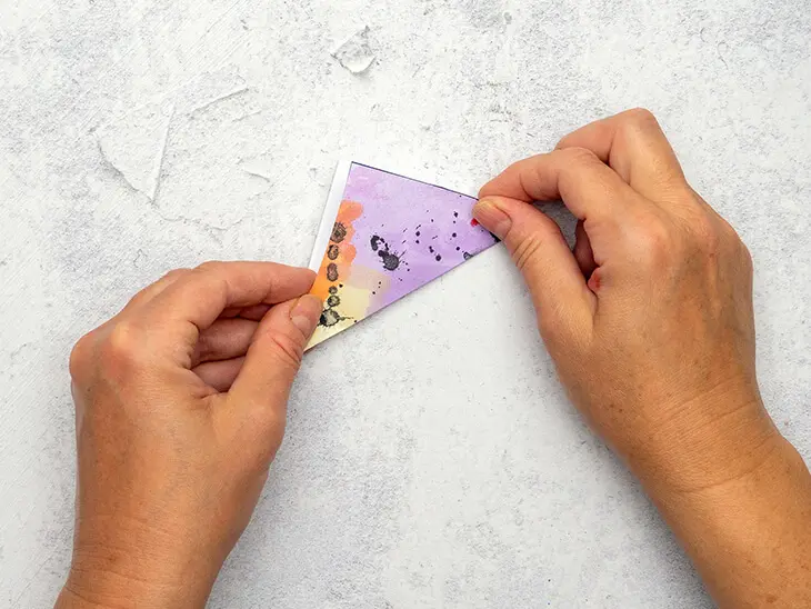 Jemand faltet ein bunt bemaltes Papierquadrat zu einem Dreieck. Foto: Johanna Rundel