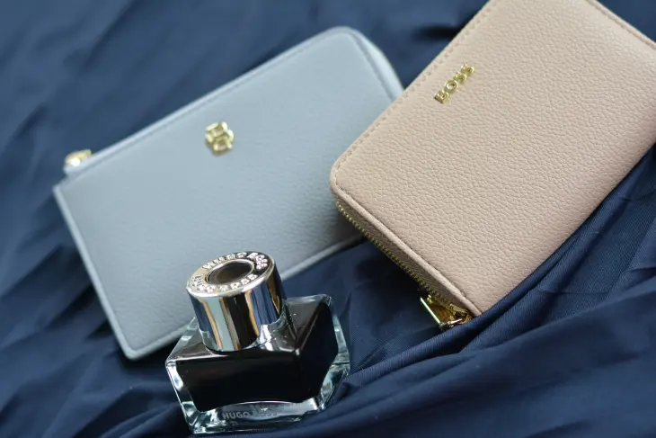 Ein Tintenfass, ein Visitenkartenmäppchen und eine Börse von HUGO BOSS liegen auf blauem Satin