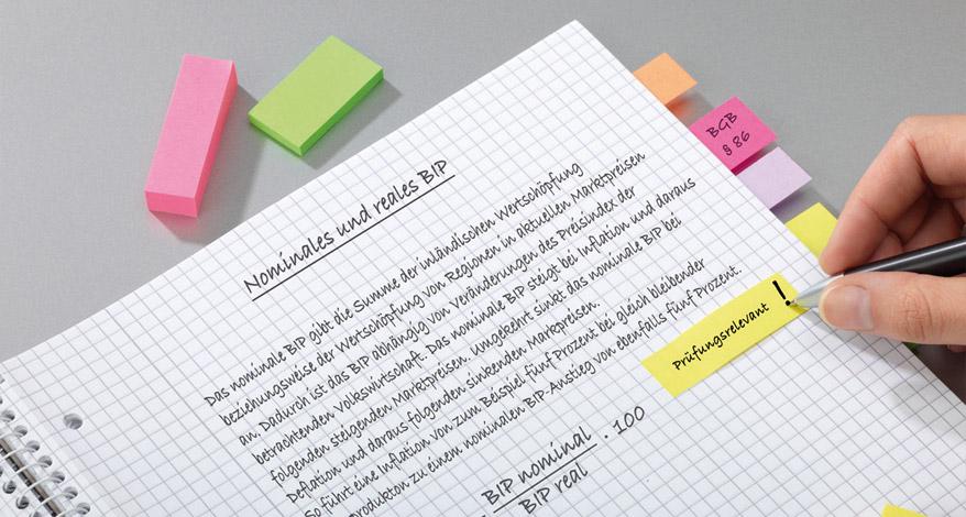Karrierter, beschriebener Collegblock, daneben bunte Post-its.