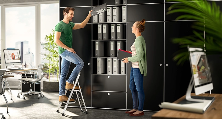 Person nutzt eine klappbare Hailo Stehleiter im Büro vor Aktenschrank.