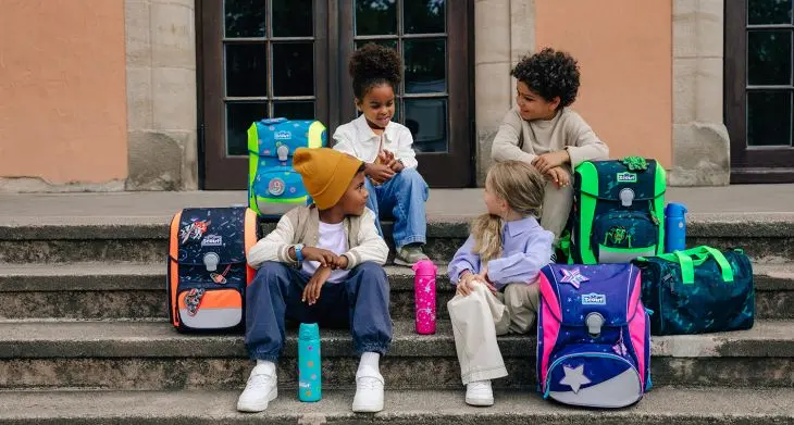 Vier Kinder sitzen mit Schulranzen von Scout auf einer Treppe und unterhalten sich.