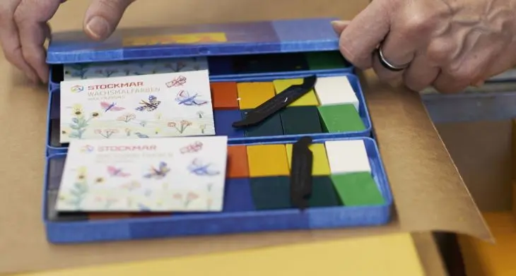 emand öffnet zwei Wachsmalblock-Verpackungen von STOCKMAR.
