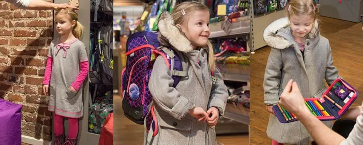 Ein kleines Mädchen wird im Geschäft für den Schulranzenkauf vermessen, trägt einen Schulranzen und bekommt ein Mäppchen gezeigt.