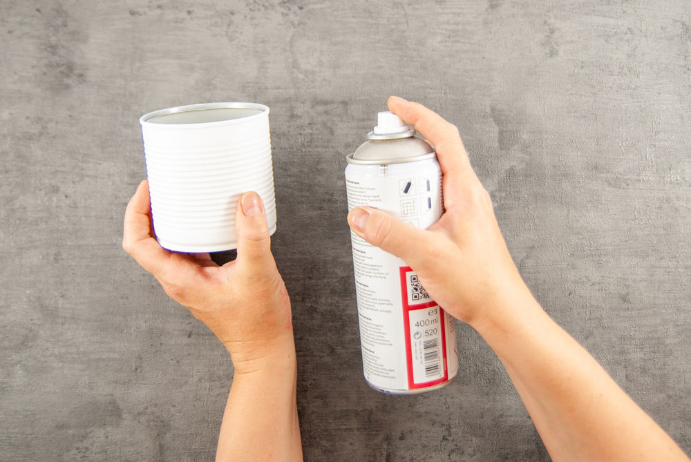 Eine Hand besprüht eine Blechdose mit weißer Farbe