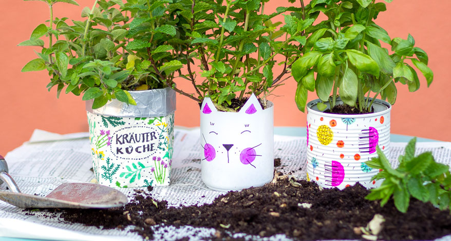 Bunte selbstgebastelte Übertöpfe auf Zeitungspapier, davor Blumenerde