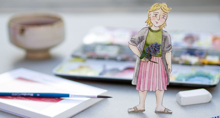 Eine kleine gestaltete Pappfigur, Farbkasten und Pinsel auf einem Tisch